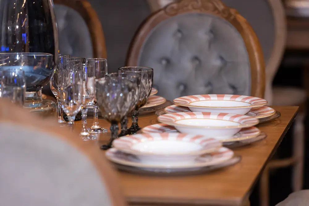 Mesa posta com louça, taças de cristal e cadeiras capitonê